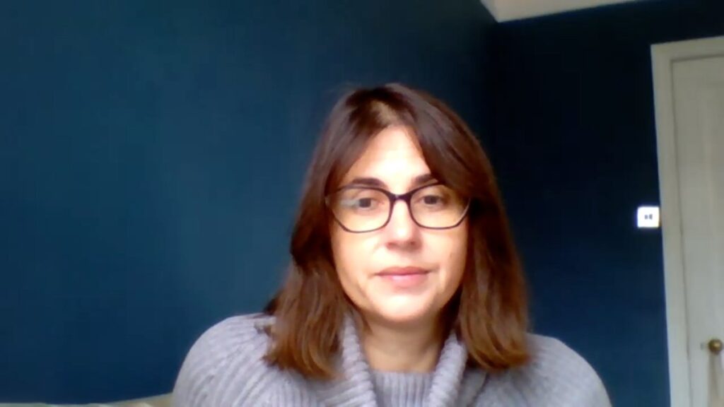 Zdjęcie autorki w okularach i szarym swetrze na tle ciemnoniebieskiej ściany